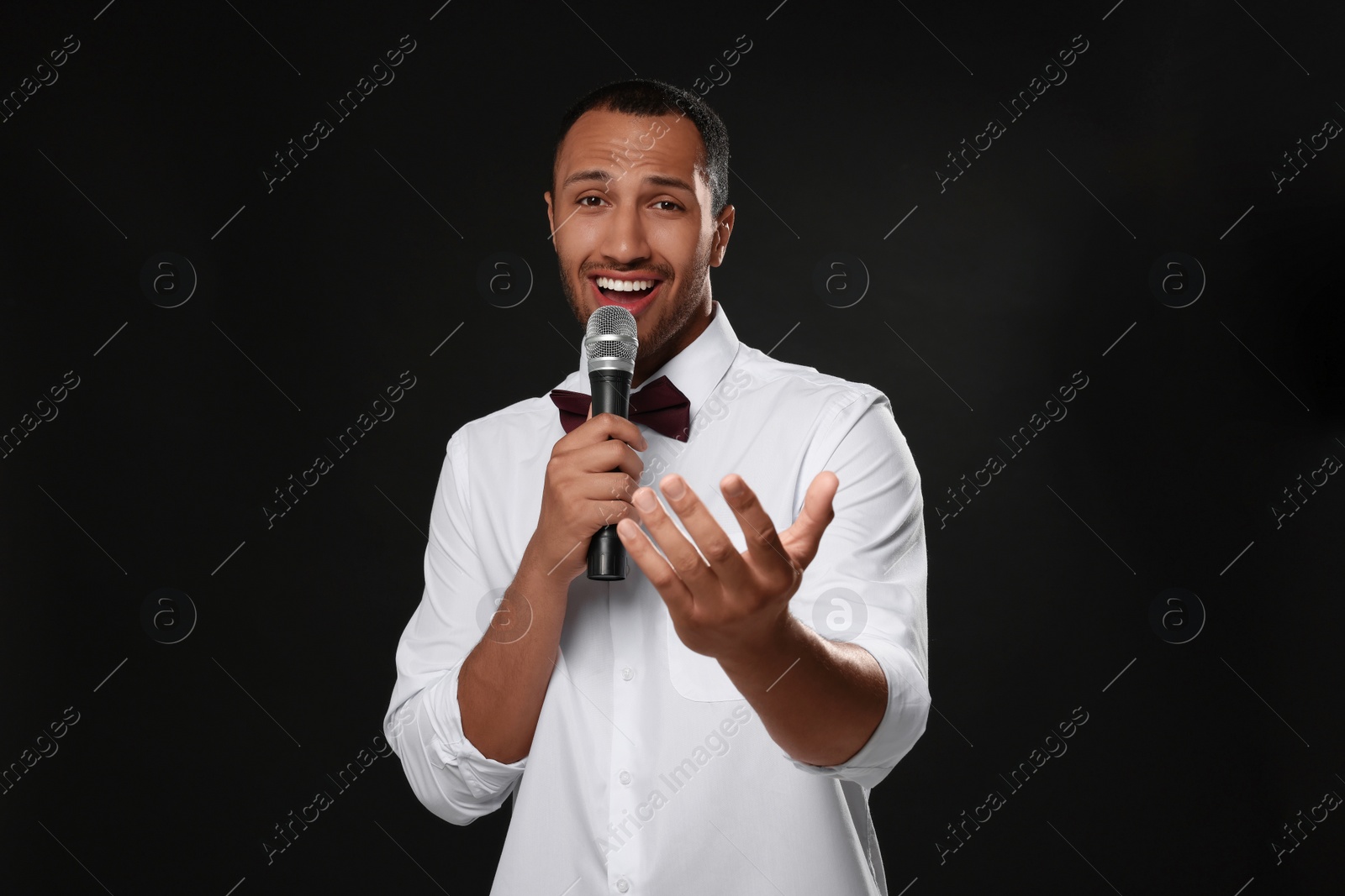 Photo of Handsome man with microphone singing on black background