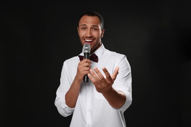 Handsome man with microphone singing on black background