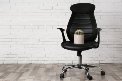 Office chair with cactus near white brick wall, space for text. Hemorrhoids concept