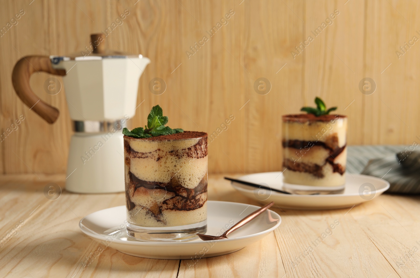 Photo of Tasty tiramisu and mint in glasses on light wooden table