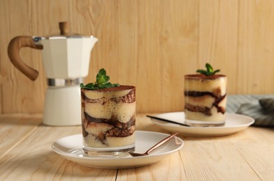 Photo of Tasty tiramisu and mint in glasses on light wooden table