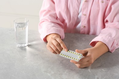 Photo of Woman taking oral contraception pill at light grey marble table indoors, closeup