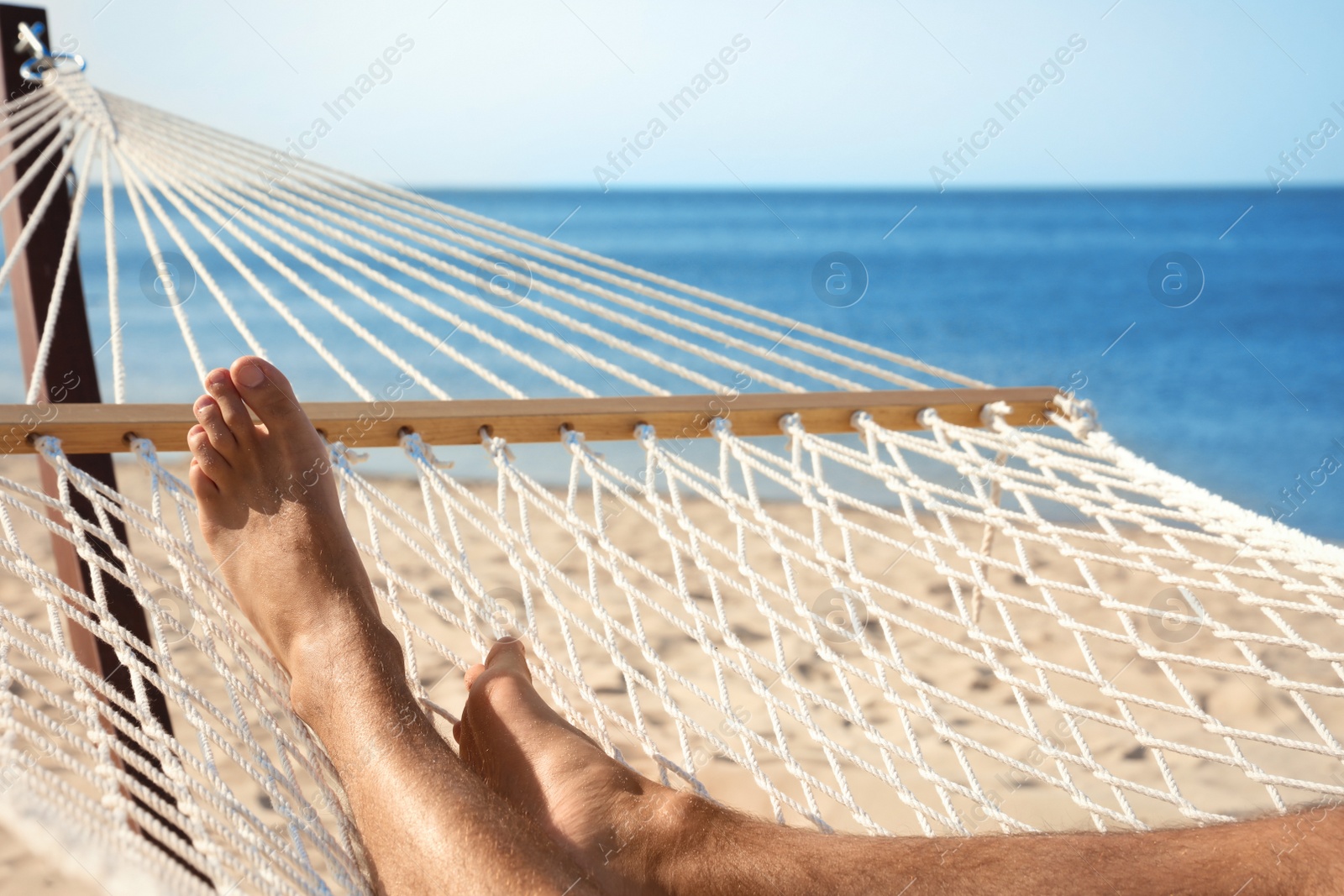 Photo of Young man relaxing in hammock on beach, closeup