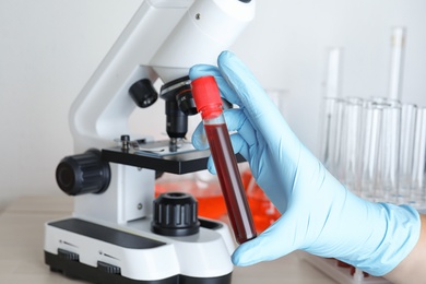 Scientist holding test tube with blood sample near microscope, closeup. Laboratory analysis