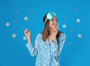 Beautiful woman wearing pajamas and sleep mask on light blue background. Bedtime