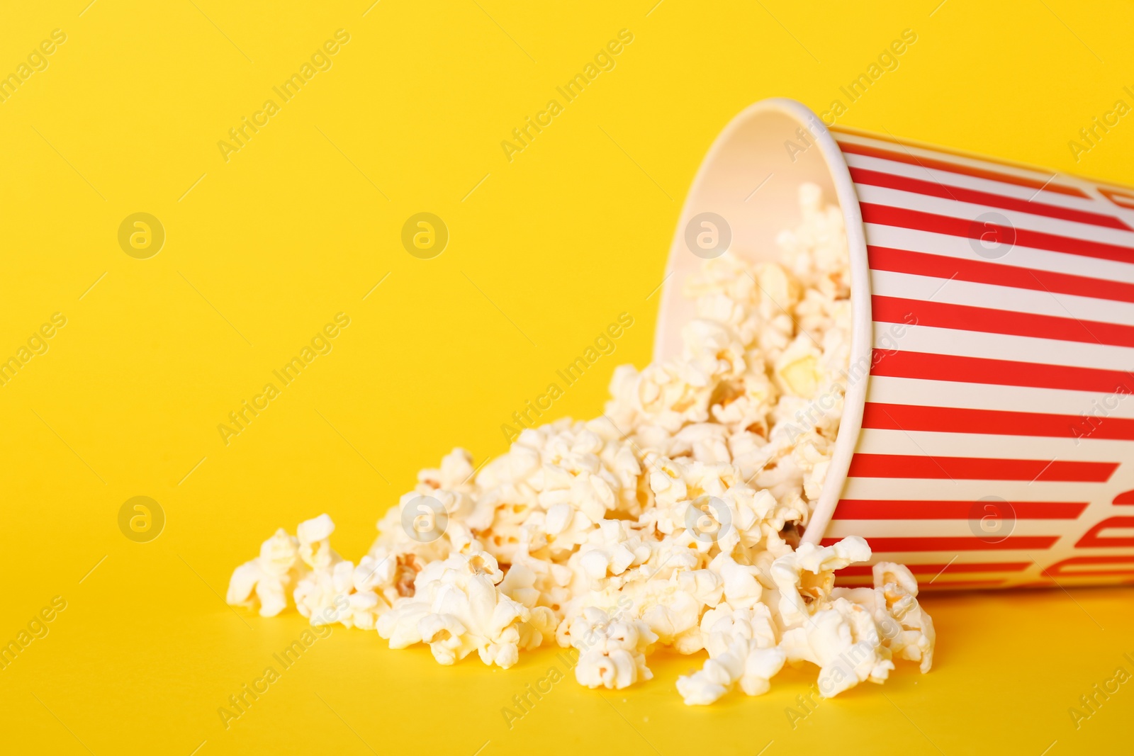 Photo of Overturned paper cup of delicious popcorn on yellow background. Space for text