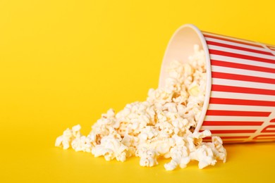 Overturned paper cup of delicious popcorn on yellow background. Space for text