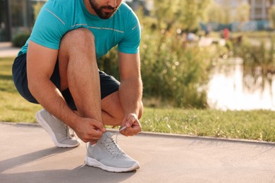 Photo of Man tying shoelaces before running in park, closeup. Space for text