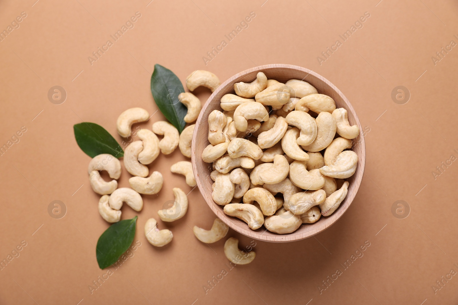 Photo of Tasty cashew nuts and green leaves on pale brown background, top view