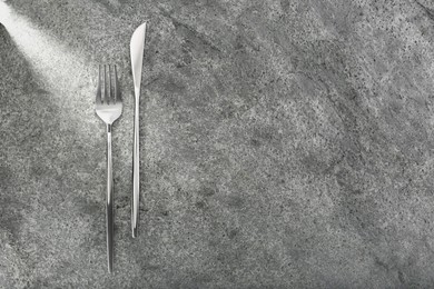 Photo of Shiny fork and knife on grey table, flat lay. Space for text