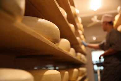 Photo of Fresh cheese heads in factory warehouse and blurred worker on background