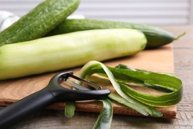 Photo of Fresh cucumbers, peels and peeler on wooden table, closeup