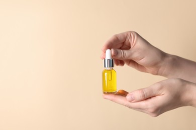 Photo of Woman holding bottle of cosmetic oil on beige background, closeup. Space for text