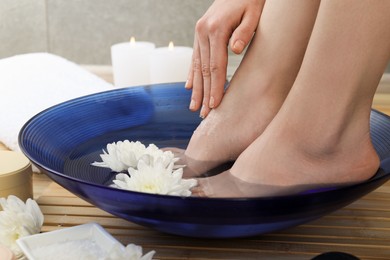 Photo of Woman soaking her feet in bowl with water and flowers on floor, closeup. Spa treatment