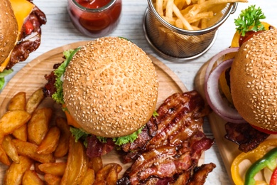 Photo of Fresh bacon burgers and fries on white wooden table, above view