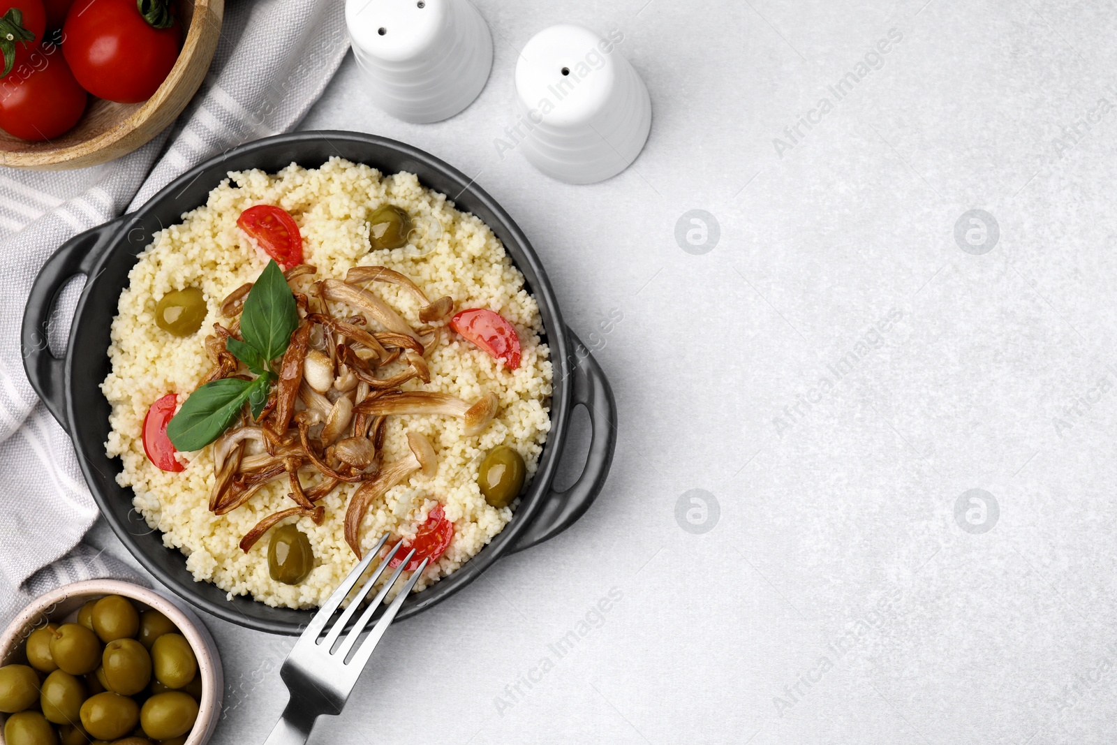 Photo of Tasty couscous with mushrooms, olives and tomatoes on grey table, flat lay. Space for text