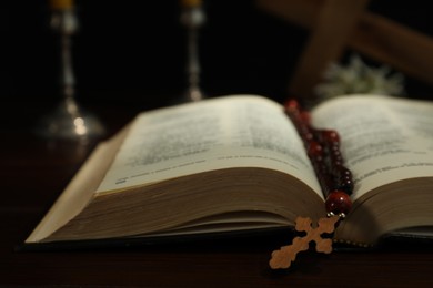 Photo of Wooden cross, rosary beads, Bible and church candles on table, closeup