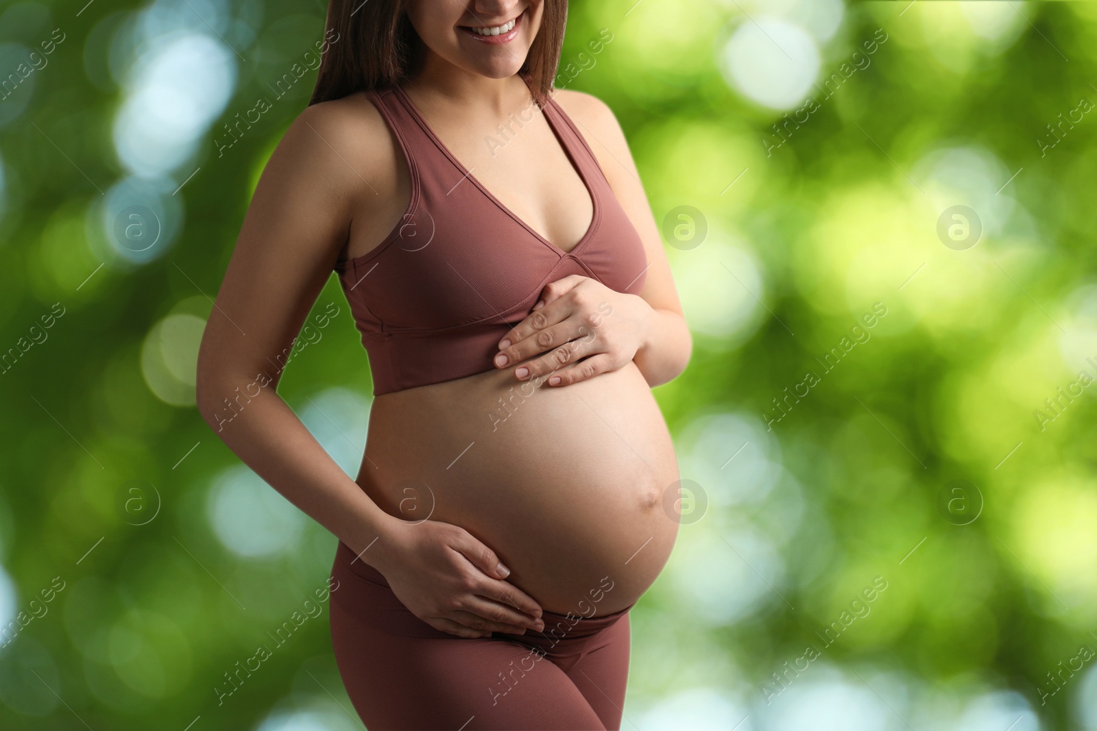 Image of Young pregnant woman touching her belly outdoors