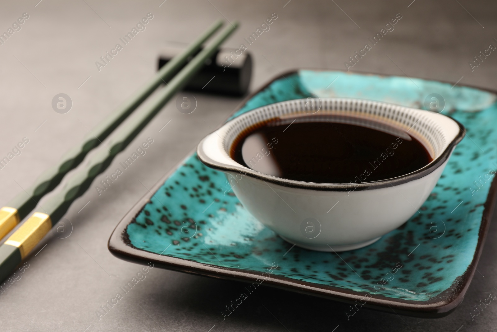 Photo of Bowl of soy sauce and chopsticks on grey table, closeup