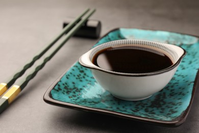 Bowl of soy sauce and chopsticks on grey table, closeup