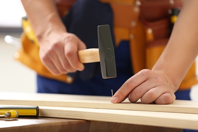 Working man hammering nail into timber indoors, closeup. Home repair