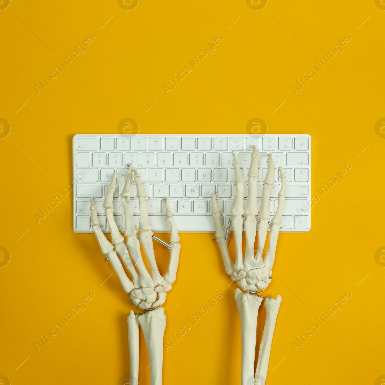 Photo of Human skeleton using computer keyboard on yellow background, top view