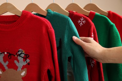 Photo of Woman choosing Christmas sweater from rack, closeup