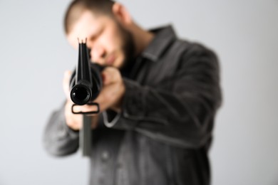 Photo of Assault gun. Man aiming rifle against light background, focus on muzzle