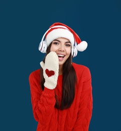 Young woman in Santa hat listening to Christmas music on dark blue background