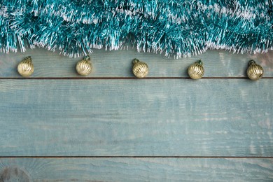 Bright tinsel and Christmas balls on light blue wooden background, flat lay. Space for text