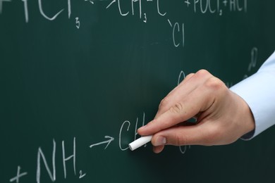 Photo of Teacher writing chemical formulas with chalk on green chalkboard, closeup