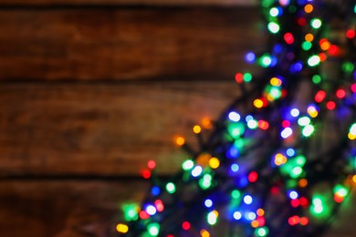 Photo of Glowing festive lights on wooden table, top view with space for text. Bokeh effect