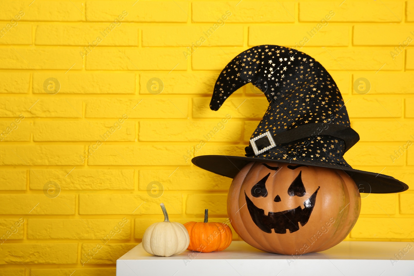 Photo of Pumpkin with drawn spooky face near yellow brick wall, space for text