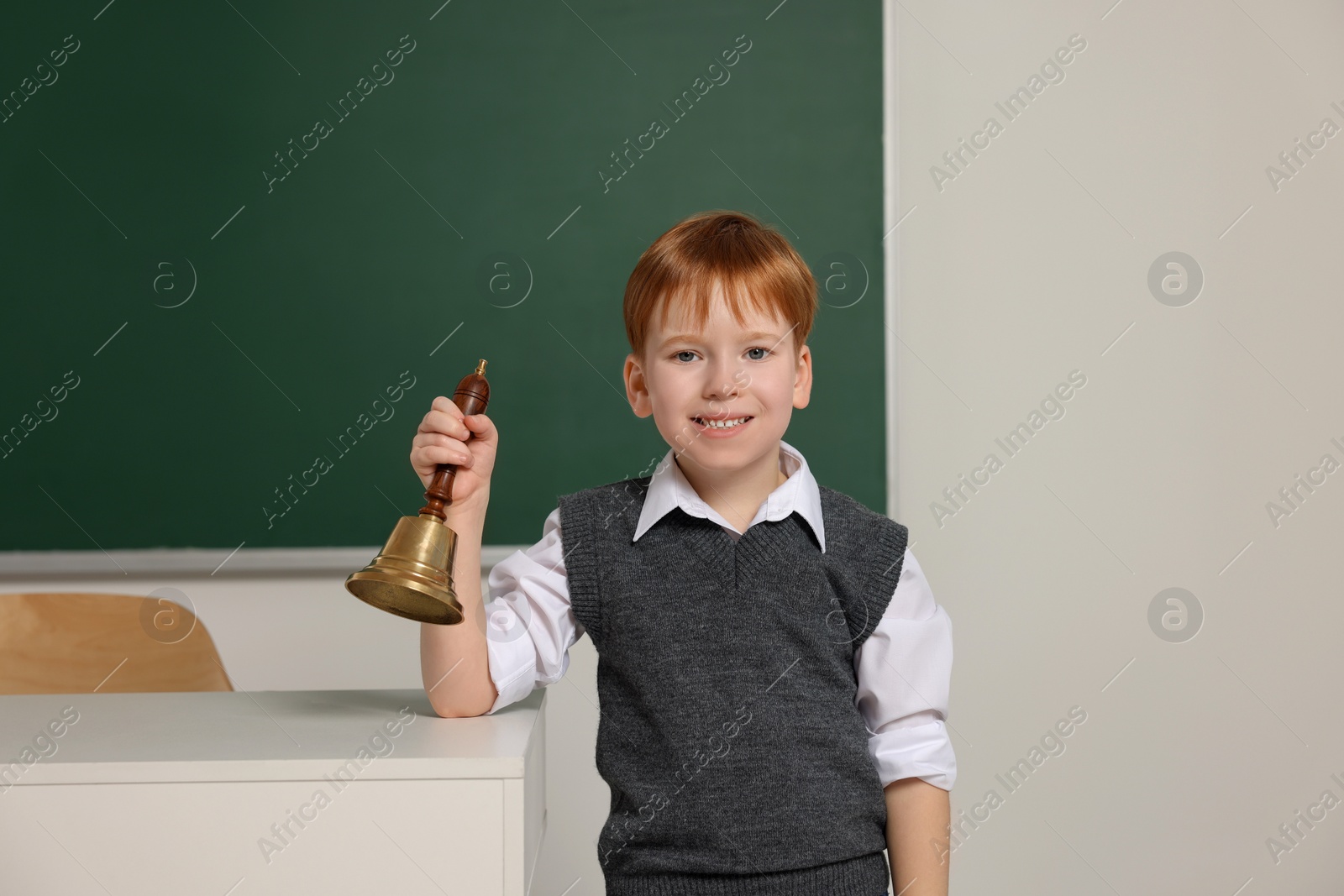 Photo of Cute little boy ringing school bell in classroom