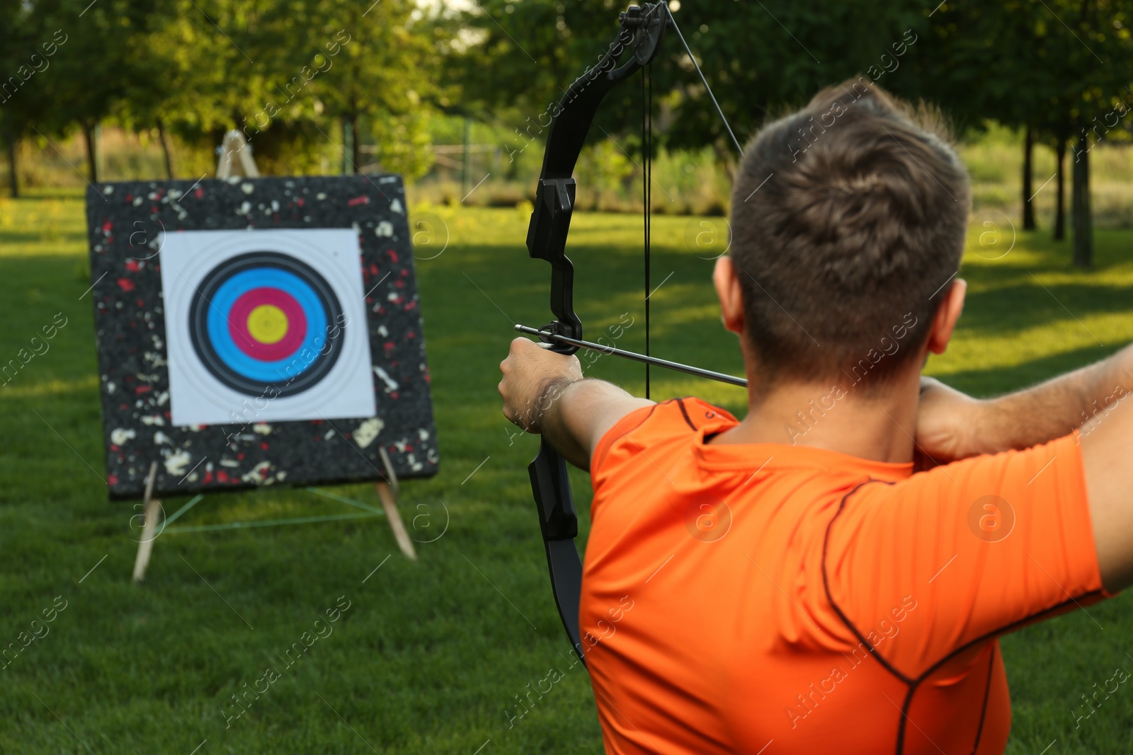 Photo of Man with bow and arrow aiming at archery target in park, back view