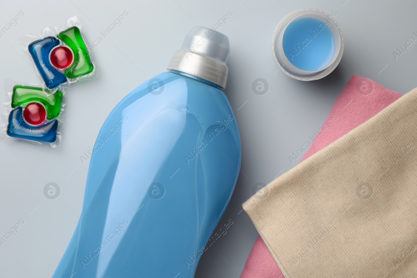 Bottle of fabric softener, laundry capsules and stacked clean clothes on light background, flat lay Photo of Bottle of fabric softener, laundry capsules and stacked clean clothes on light background, flat lay