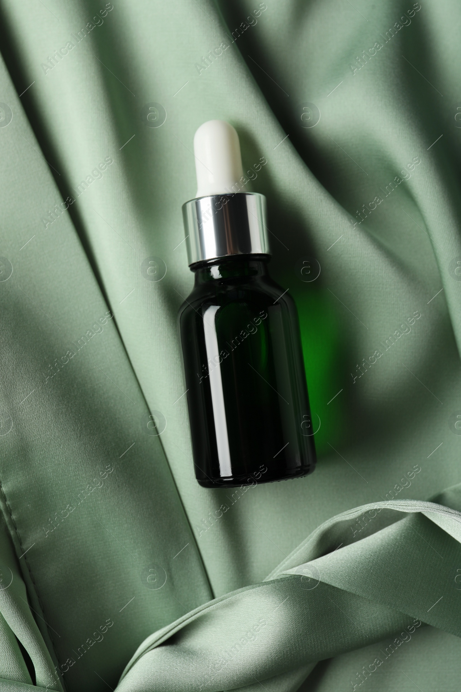 Photo of Bottle of hydrophilic oil on green fabric, top view