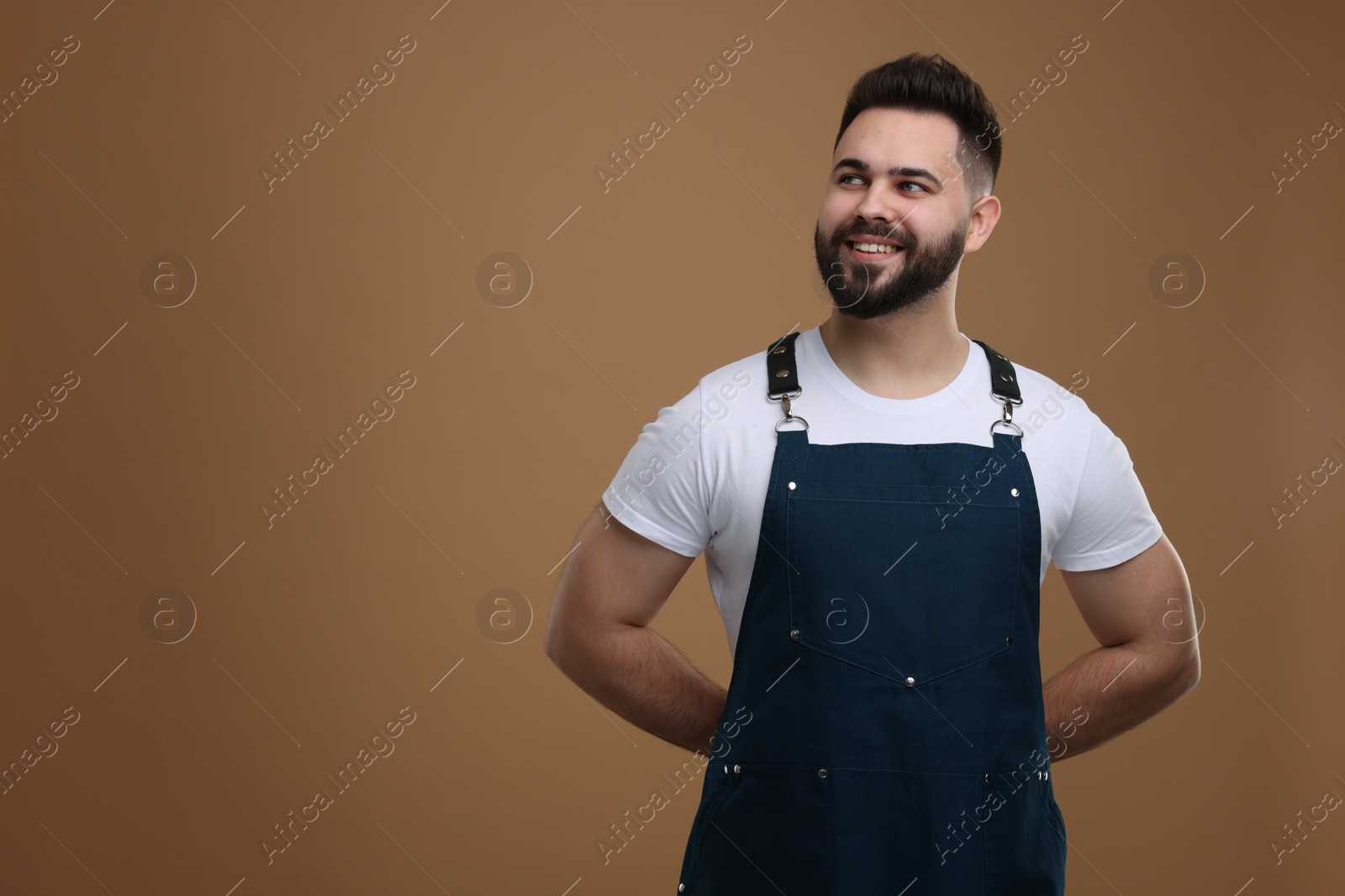 Photo of Smiling man in kitchen apron on brown background. Mockup for design