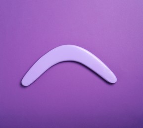 Lilac wooden boomerang on purple background, top view