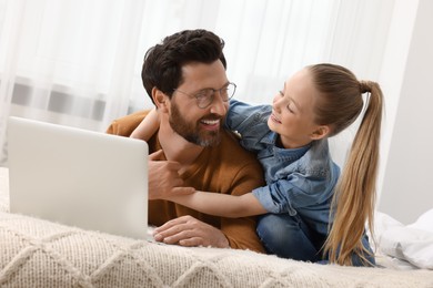 Happy man and his daughter with laptop on bed at home