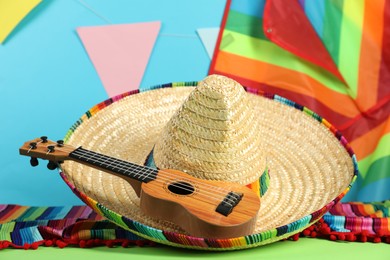 Mexican sombrero hat, poncho and ukulele on green table, closeup