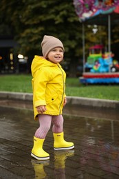 Photo of Happy little girl walking in puddle outdoors