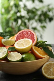 Different fresh citrus fruits and leaves on table against blurred background, closeup