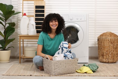 Photo of Happy woman with laundry near washing machine indoors