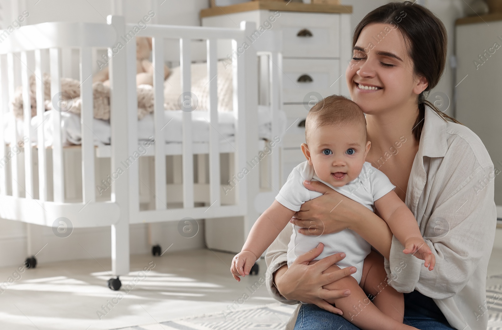 Photo of Happy young mother with her baby in nursery. Space for text