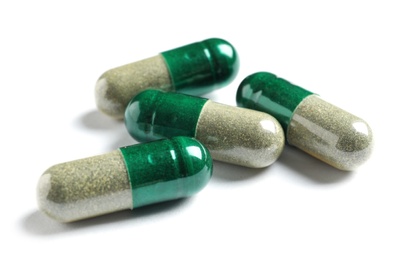 Photo of Green spirulina capsules on white background. Alternative medicine