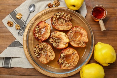 Photo of Tasty baked quinces with walnuts and honey in bowl on wooden table, flat lay