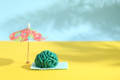 Photo of Brain made of plasticine on mini blanket under umbrella against color background, space for text