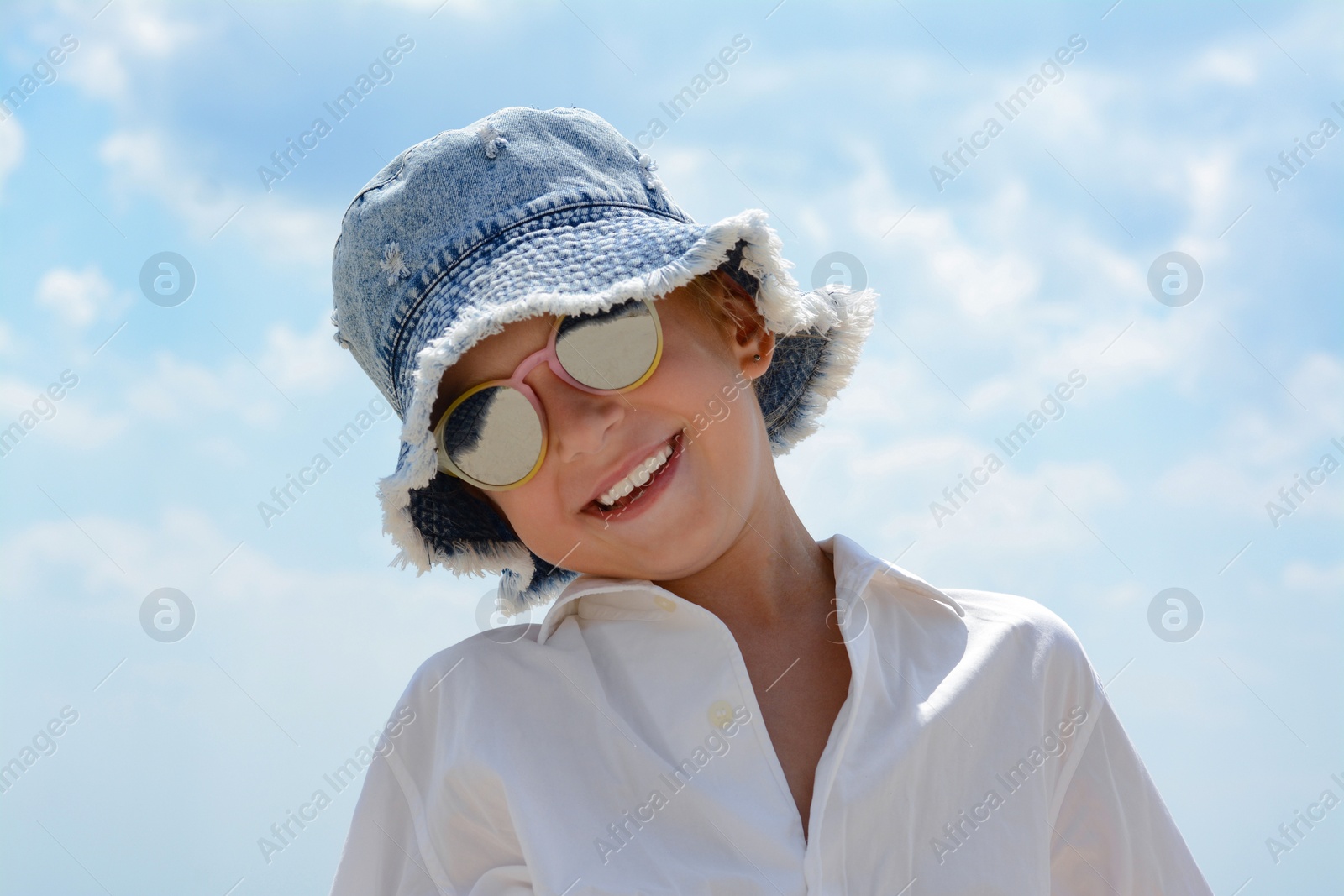 Photo of Little girl wearing sunglasses and hat at beach on sunny day