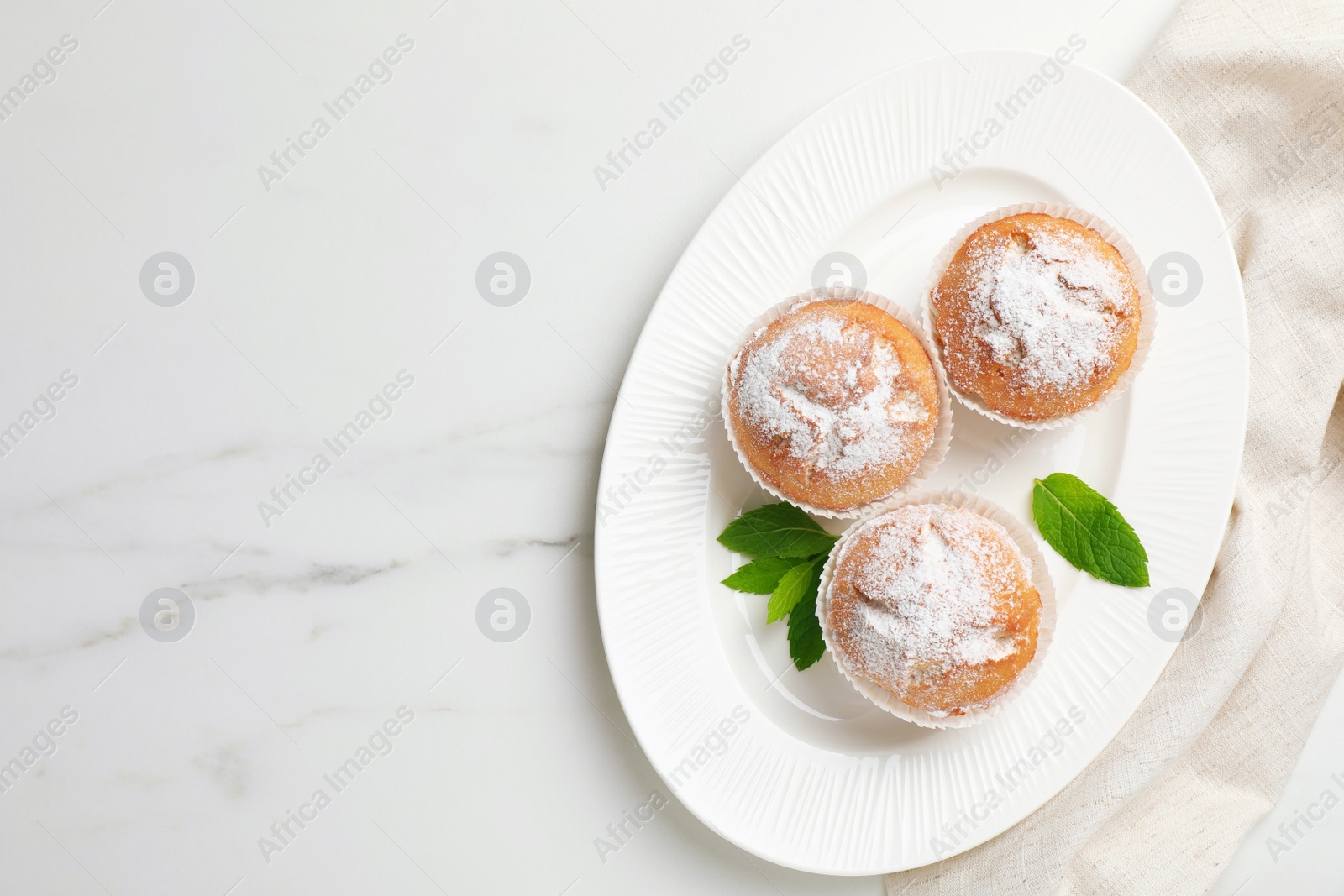 Photo of Tasty homemade muffins served with mint on white marble table, top view. Space for text